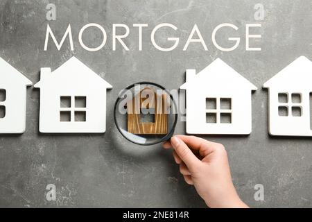 Mortgage concept. Woman with magnifying glass and different house models on grey stone background, top view Stock Photo