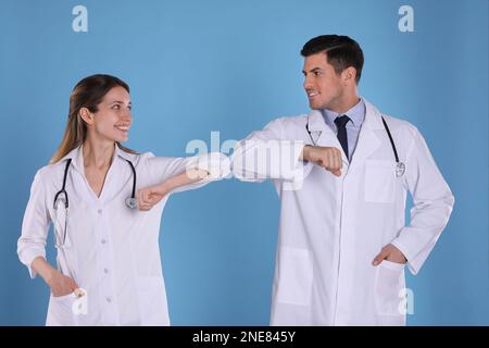 Doctors greeting each other by bumping elbows instead of handshake on light blue background Stock Photo