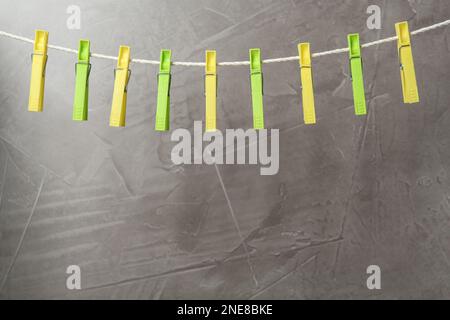Colorful plastic clothespins on rope against grey stone background. Space for text Stock Photo