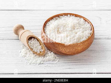 Coconut flakes in wooden bowl with scoop on white wooden background Stock Photo