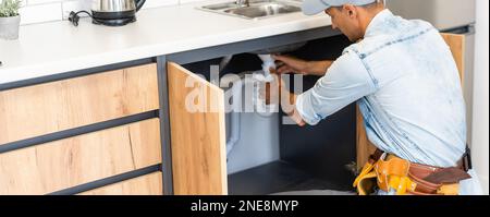 plumber fixes sink siphon by two pipe-wrenches in kitchen. Stock Photo