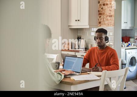 Young multiracial couple working online from home in their kitchen Stock Photo