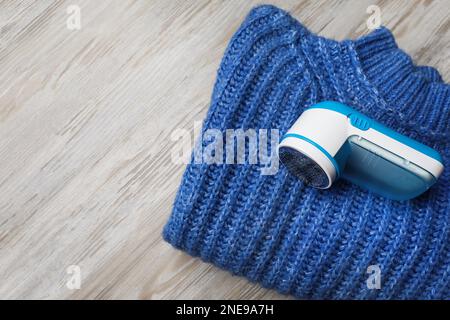Modern fabric shaver for lint removing and sweater on wooden table, top view Stock Photo