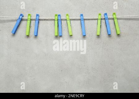 Colorful plastic clothespins and rope on light grey stone background. Space for text Stock Photo