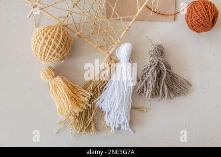 On table are materials and blanks (multi-colored woolen threads, wooden frame, tassels made of multi-colored thread) for creative activity of designer Stock Photo