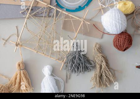 On table are materials and blanks (multi-colored woolen threads, wooden frame, tassels made of multi-colored thread) for creative activity of designer Stock Photo