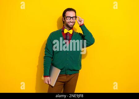 Photo of young programmer expert it developer guy wear green jumper with plaid shirt touch glasses hold netbook isolated on yellow color background Stock Photo