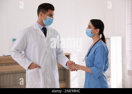 Doctors with protective masks giving handshake in clinic Stock Photo
