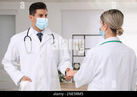 Doctors with protective masks giving handshake in clinic Stock Photo