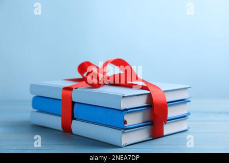 Different books tied with red ribbon on light blue wooden table Stock Photo