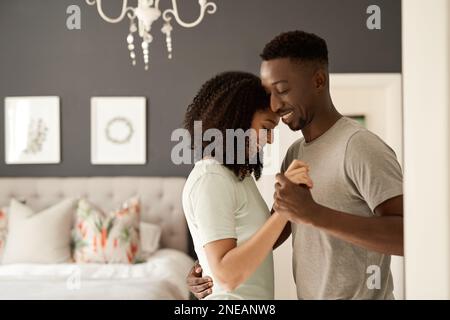 Smiling young multiracial couple dancing together in their bedroom Stock Photo