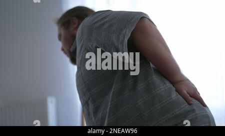 One overweight man having back pain by getting up from couch. A sedentary fat male person having physical injury Stock Photo