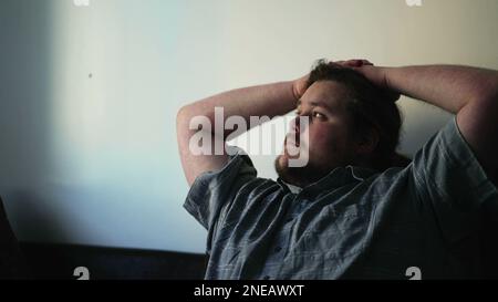 One pensive overweight young man thinking deeply at home. Thoughtful male caucasian person looking out window with meditative expression Stock Photo