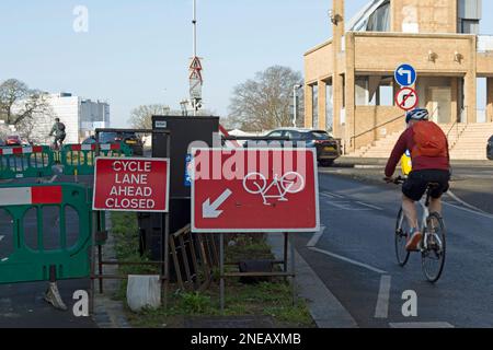 a cyclist passes an upside down cycle direction side adjacent to a cycle lane ahead closed sign on the approach to kingston bridge, kingston, england Stock Photo