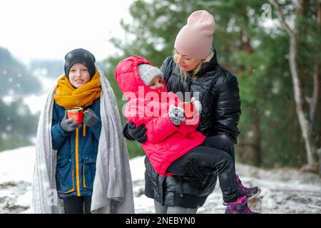 Portrait of wonderful family standing outside in forest in snowy winter. Middle-aged woman mother holding little girl. Stock Photo