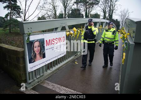 Police officers walk past a missing person appeal poster for Nicola Bulley and yellow ribbons and messages of hope tied to a bridge over the River Wyre in St Michael's on Wyre, Lancashire, as police continue their search for Ms Bulley, 45, who vanished on January 27 while walking her springer spaniel Willow shortly after dropping her daughters, aged six and nine, at school. Picture date: Thursday February 16, 2023. Stock Photo