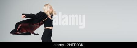 young blonde woman in stylish black outfit jumping isolated on grey, banner,stock image Stock Photo