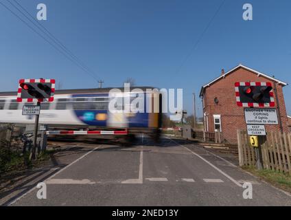 24 March 2022 - A moving train passing over an automatic half barrier level crossing on clear day with blue sky. Stock Photo