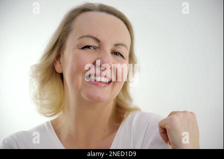 tenderness pleasure on face of sly look of middle-aged woman sincere smile raised one shoulder up looks askance coquetry pretty woman on white background pleasant product purchase excellent emotion Stock Photo