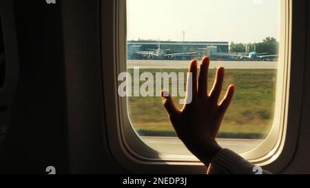 Kid s hand touching airplane window, close up. Silhouette of a child's palm against the background of a window in an airplane. The concept of safety of flights. High quality photo Stock Photo