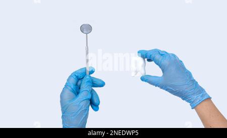 Female dentist hand holds a model tooth and dentist mirror. Light background. Concept of oral hygiene in the family. Stock Photo