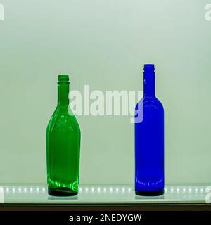 Two colorful bottles of different shapes and colors on glass shelf with highlights from lights. Still life in minimalist style Stock Photo