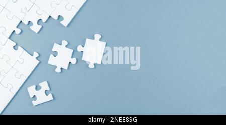 top view of white blank unfinished jigsaw puzzle on blue background, completing a task or solving a problem concept Stock Photo