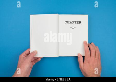 top view of person fiipping open a book with text CHAPTER 1 on first page against blue background Stock Photo