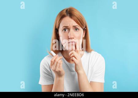 Upset woman with herpes applying cream on lips against light blue background Stock Photo