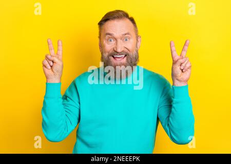 Photo portrait of handsome granddad showing double v-sign excited cheerful dressed stylish cyan outfit isolated on yellow color background Stock Photo