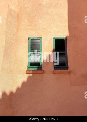 Abstract sun and shadow pattern cast on a rustic terracotta colour wall with traditional green wooden shutters, tropical hot summer vacation concept Stock Photo