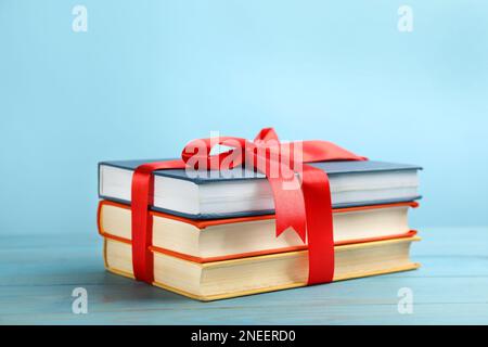 Different books tied with red ribbon on light blue wooden table Stock Photo