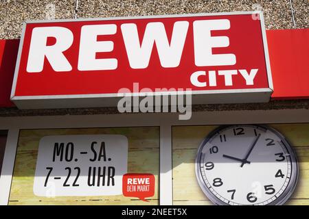 Hannover, Germany - March 17, 2020: Rewe City logo sign and opening times or business hours at local branch of german supermarket chain Stock Photo