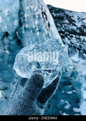 Closeup of gloved hand with glove holding frozen, transparent chunk of Glacial ice from an Icelandic Glacier, Nordic icy Winter scene POV Stock Photo