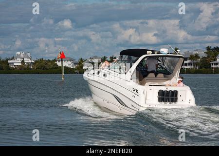 motorboat underway, approaching marker, 4 people, leisure, recreation, wake, houses on shore, Chaparral, cabin cruiser, marine, motion, MR Stock Photo