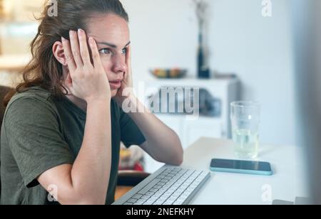 Surprised woman holding head with her hands looking at screen of computer while sitting at desk. Stock Photo