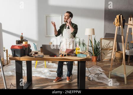 Cheerful carpenter talking on smartphone near tools on working table in studio,stock image Stock Photo