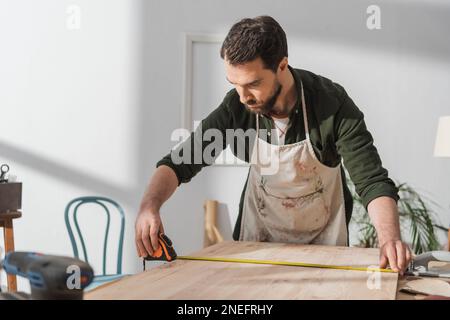 Brunette restorer measuring wooden board on table,stock image Stock Photo