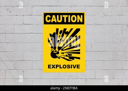Yellow warning sign screwed to a brick wall to warn about a threat. In the middle of the panel, there is a explosion symbol and the message is saying Stock Photo