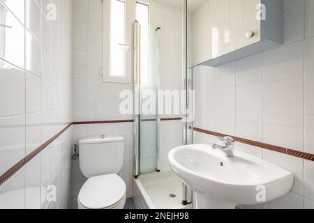 Luxury bathroom is lined with white ceramic tiles with shower toilet and sink with a narrow vertical windows for natural light. Concept of compact but Stock Photo