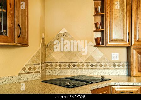 A tile mountain motif is used as a backsplash behind an electric flat glass cooktop in a kitchen remodel with wood cabinets in a contemporary kitchen. Stock Photo