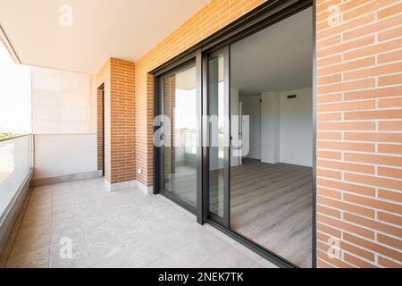 Side view of terrace opening after the large panoramic windows in luxury apartment of new building made of red brick and black metal frames. Concept Stock Photo