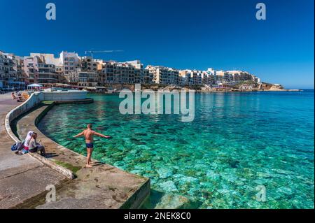 Man dives into the turquoise waters of Marsalforn village, Gozo Stock Photo
