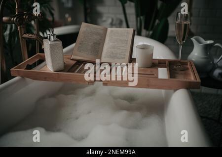 Native hues organic shapes look of bathroom with big window oval bathtub in neutrals earth tones. Green palm plants candles bubblebath leasure and rel Stock Photo