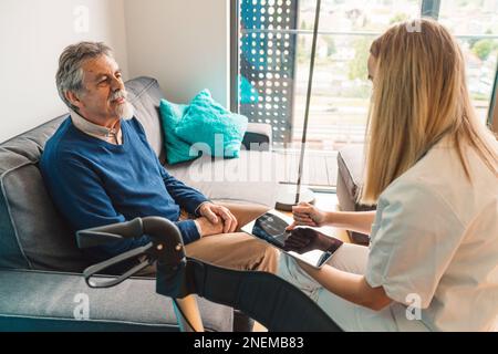 Nurse sitting on the chair across the senior man sitting on the sofa carefully listening to her  Stock Photo