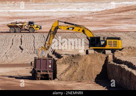 A heavy duty excavator loads a container truck with hazardous uranium tailings at the UMTRA remediation project, Moab, Utah. Stock Photo