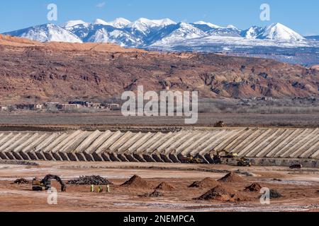 A heavy duty excavator loads a dump truck with hazardous uranium tailings at the UMTRA remediation project, Moab, Utah.  The snow-capped La Sal Mounta Stock Photo