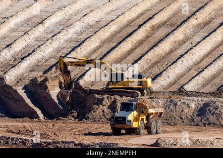 A heavy duty excavator loads a dump truck with hazardous uranium tailings at the UMTRA remediation project, Moab, Utah. Stock Photo