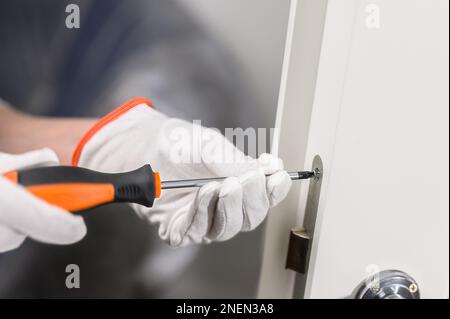 men's hands with a manual screwdriver and a screw handle on a white door. Door lock attachment. Stock Photo