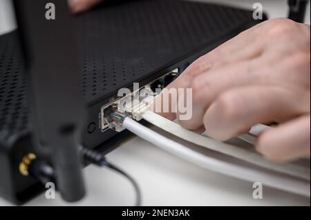 A woman's hand connects an internet cable to a router socket. Fast and wireless internet concept Stock Photo